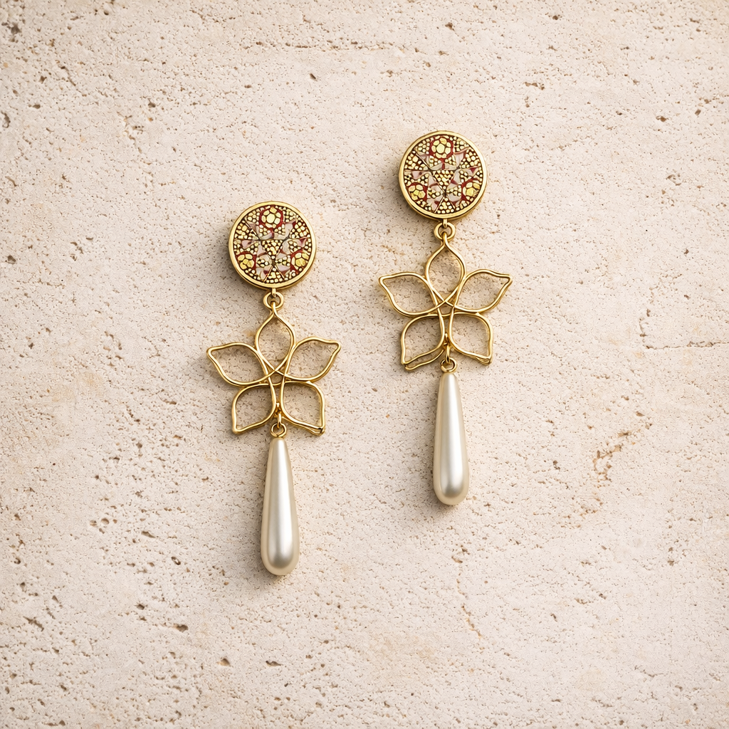 Gold earrings with floral designs and pearl drops on a beige surface