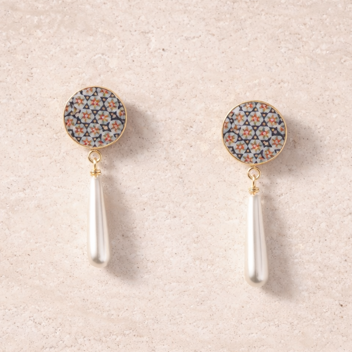 Pair of earrings with decorative tops and white stems on a beige background