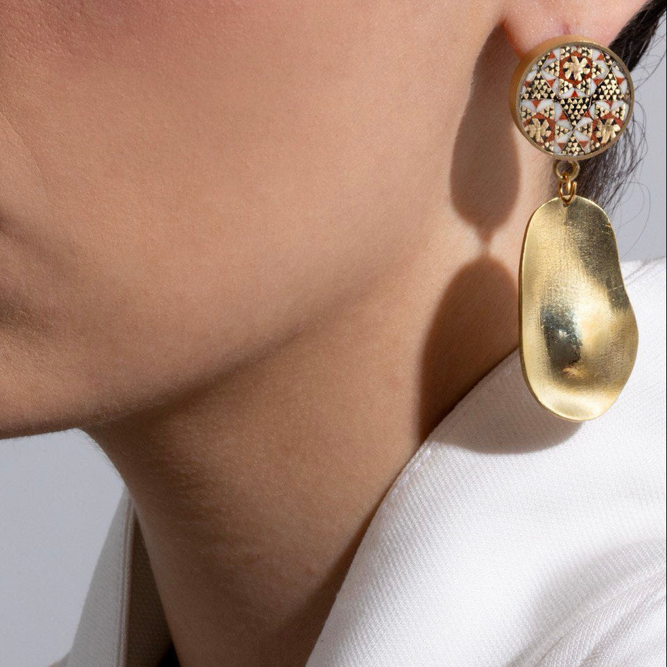 Close-up of a person wearing a gold earring with a textured top and smooth bottom.